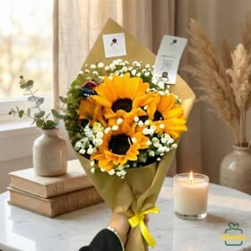 Hand-held sunflower bouquet wrapped in brown paper with baby’s breath flowers, placed in a cozy indoor setting.
