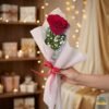Single red rose bouquet wrapped in white paper with baby’s breath, held in hand, perfect romantic gift in Pakistan