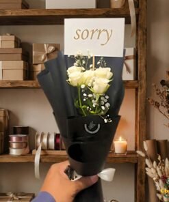 Single sorry flower bouquet wrapped in black paper with white roses and a “sorry” card
