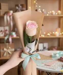 Single pink rose bouquet wrapped in kraft paper with mint ribbon, held by hand