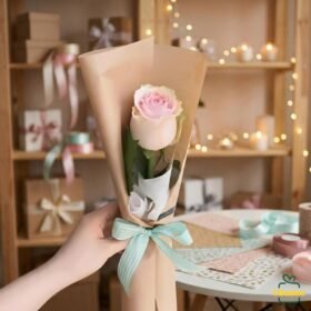 Single pink rose bouquet wrapped in kraft paper with mint ribbon, held by hand