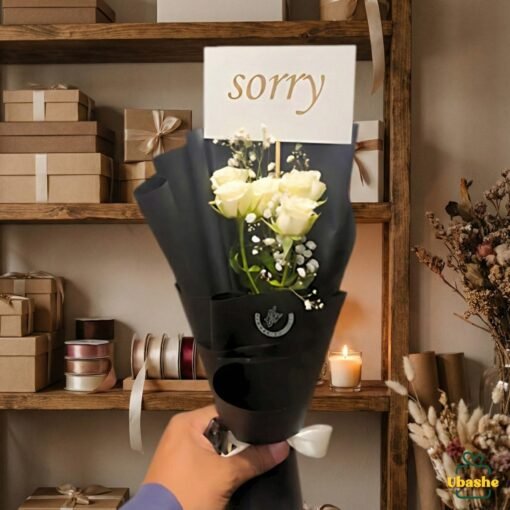 Single sorry flower bouquet wrapped in black paper with white roses and a “sorry” card